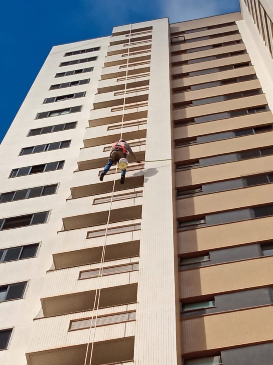 Pintor de rapel descendo a fachada lateral de edifício residencial