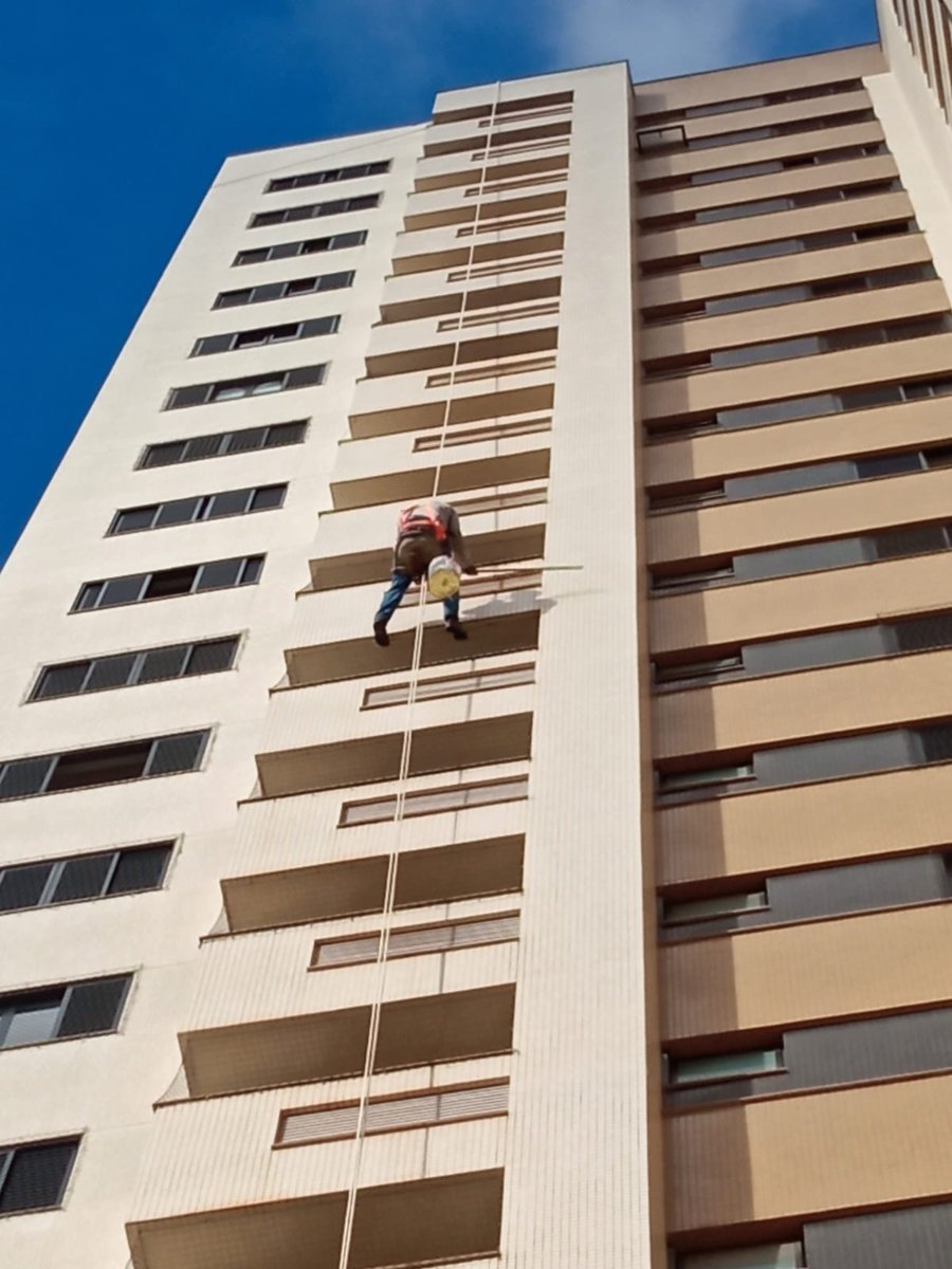 Pintor aplicando rolo extensor com tinta bege na fachada do edifício