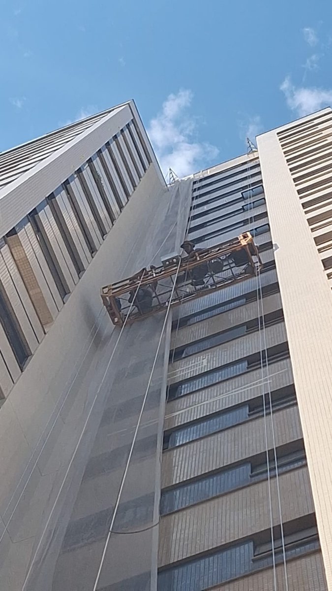 Trabalho vertical de pintura externa predial com rolo e balancim